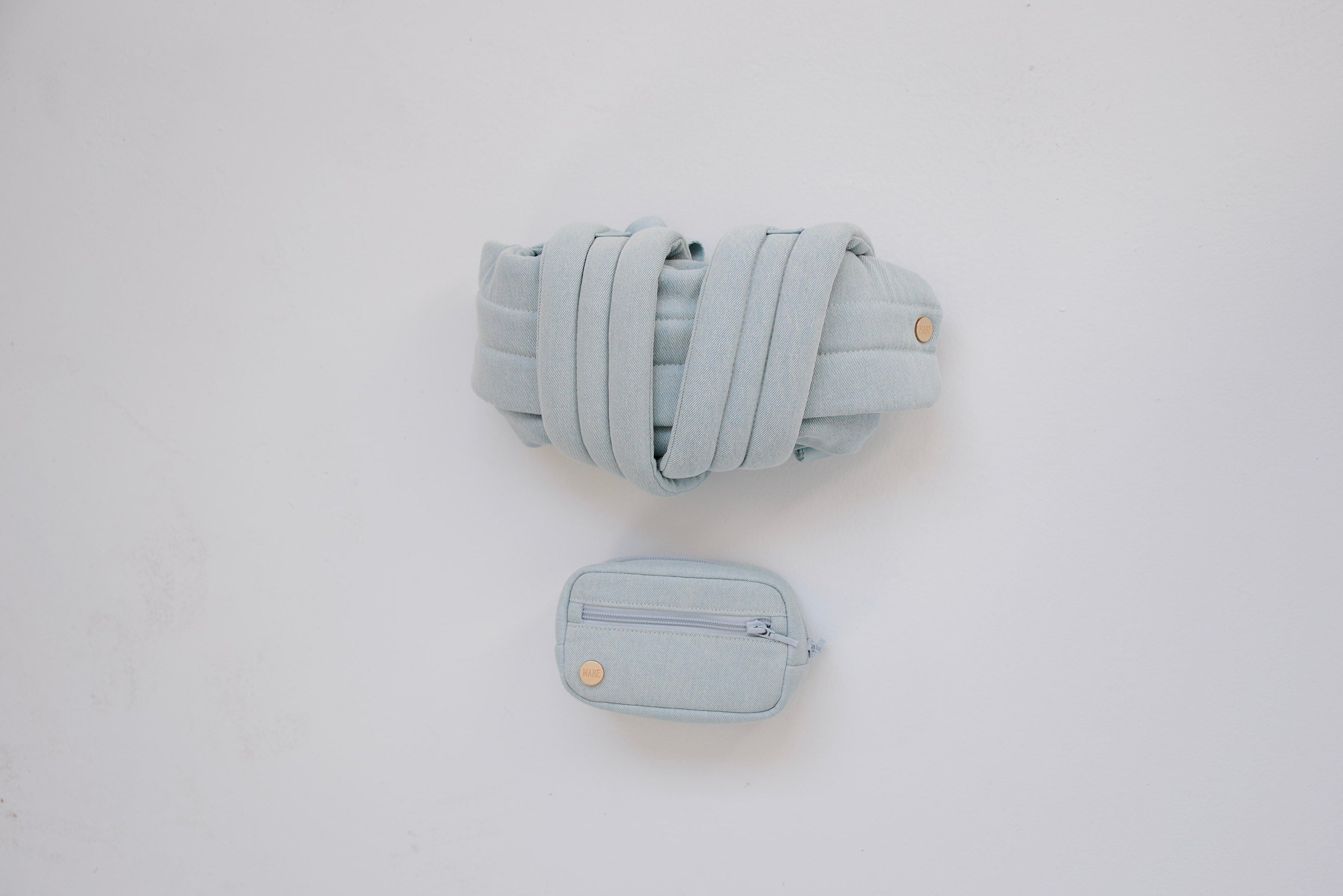 Rolled-up light blue denim Mabē Monarch buckle carrier with a matching accessory bag on a white background