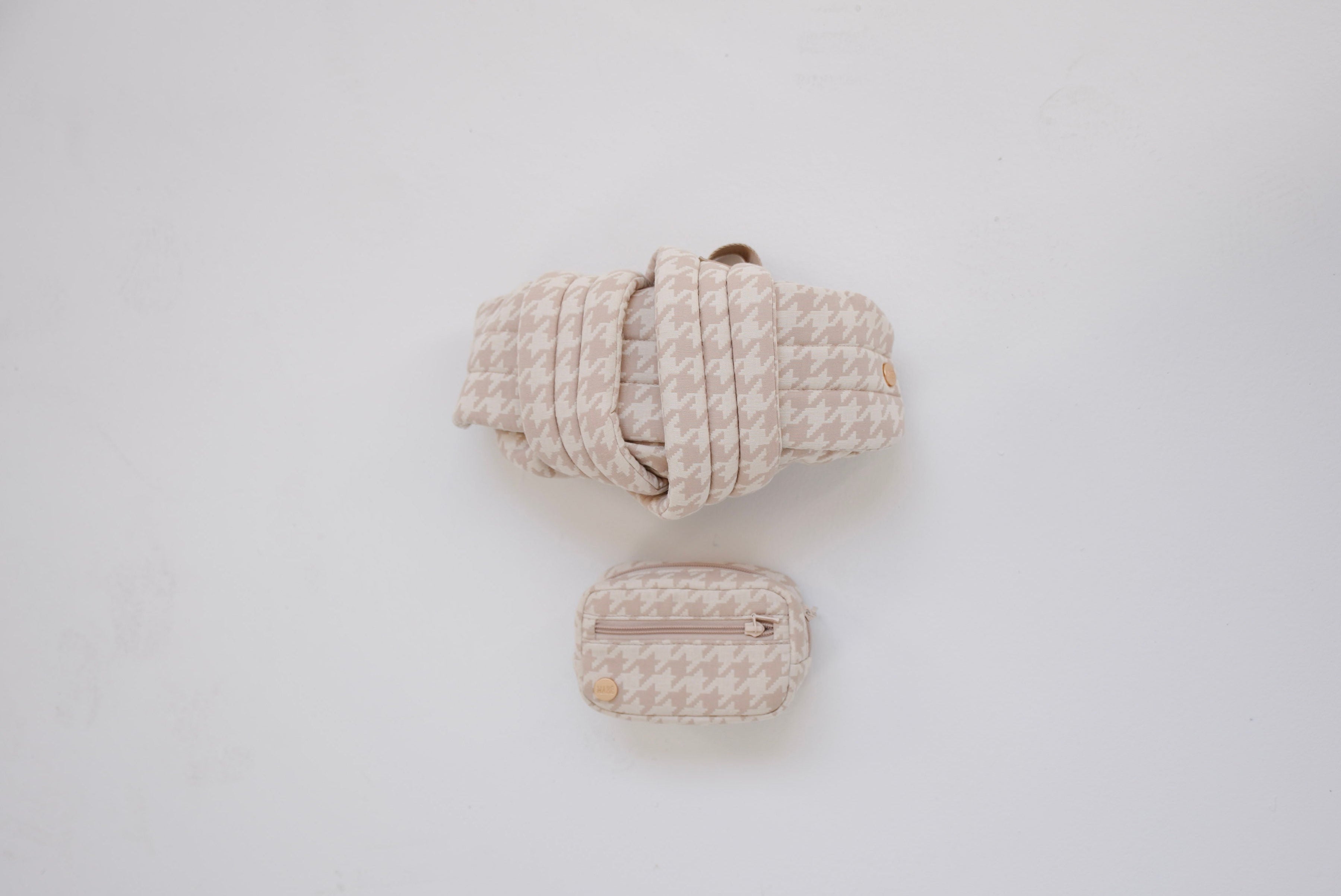 Rolled-up beige houndstooth patterned Mabē Monarch buckle carrier with a matching accessory bag on a white background