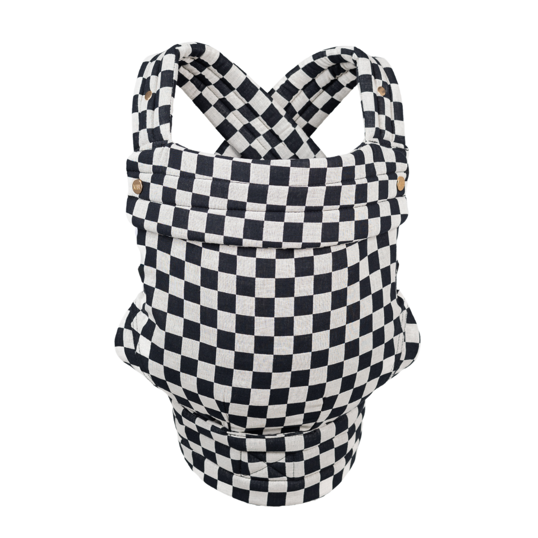 The Mabē Monarch Carrier, front view, alone on a white background. The carrier has crossed straps for across the back and a fold-down head support flap with snaps. This colorway is Ebony Check, which is black and white checkered.